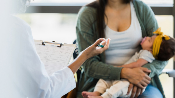 Mother holds baby while speaking to a doctor at a wellness check-up.