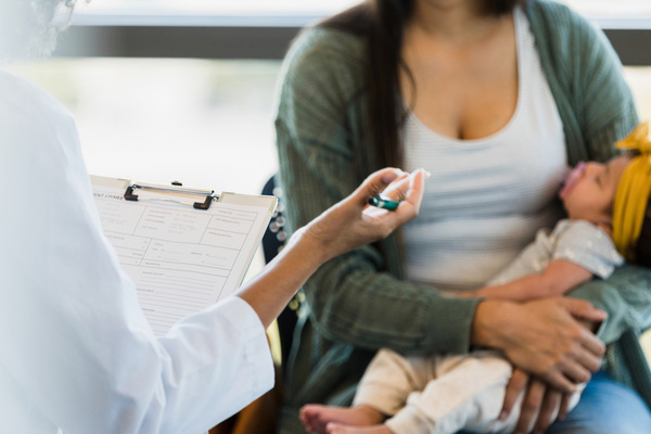 Mother holds baby while speaking to a doctor at a wellness check-up.